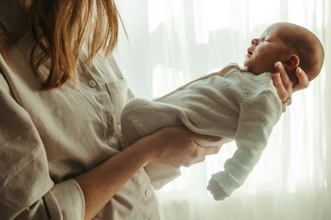 Hands holding a newborn in soft daylight