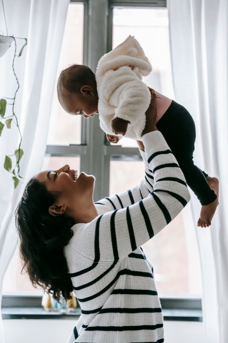 A mum lifting her baby up by a bright window