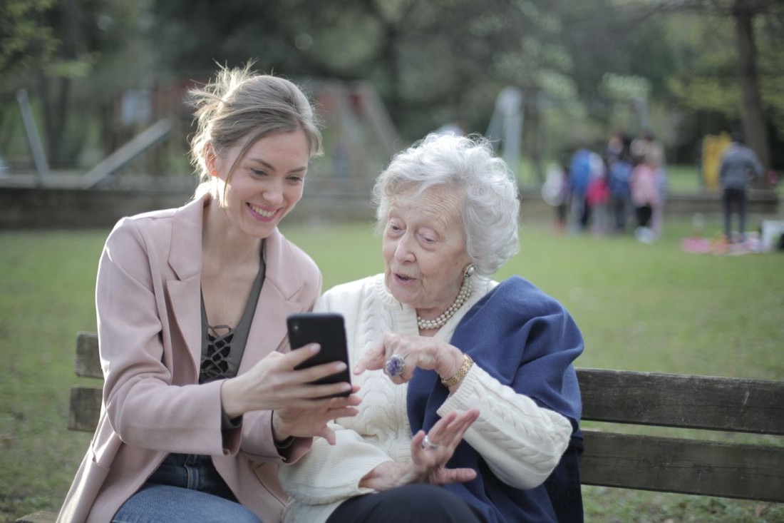 An older mum and her adult daughter smiling at a phone together